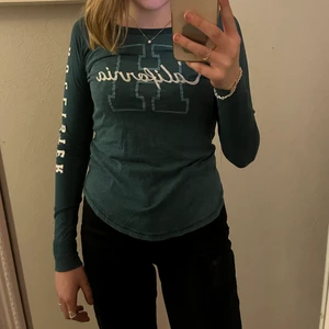 Hollister tröja grön - Aldrig använd. Mörkgrön tröja med vitt tryck. Tyget är ganska tunt och fläktar. Storlek M men passar som en S. Jag är 169 cm lång och har normalt storlek S i tröjor 
