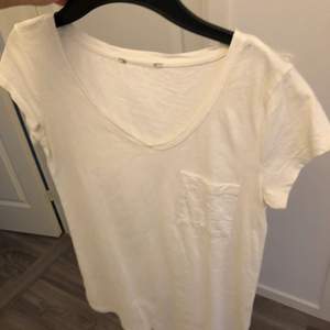 En vit T-shirt i skjort material. V ringad och bröstficka. Storlek S