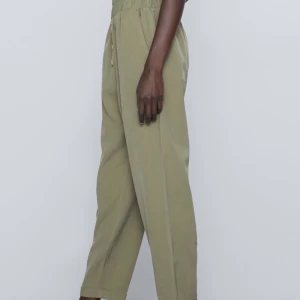 Byxa med hög midja  - Högmidjad khaki byxa med sidfickor, är lite pösig, uppvikt nederkant