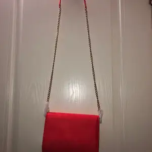En röd väska med guldiga detaljer från HM. Har inte använt en ända gång och prislappen sitter fortfarande på. Väskan har en ficka på insidan av den och rymmer det som behövs. Den är som sagt aldrig använd och är helt ny. Kedjan går att ta bort från själva väskan.