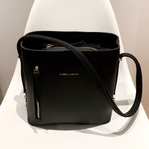 Laura Ashley väska - Snygg väska från Laura Ashley i svart med snygga guld detaljer. Axelremmen kan justeras till tre olika längder genom att flytta ändarna till olika hakar (se bild). 3 innerfack och 2 ytterfack. Sparsamt använd och tar väl hand om mina väskor. Mått: 25x26x15 cm. Nypris 1,699kr 📦 Hämtas i Skanstull / skickas mot porto. Rökfritt & Djurfritt hem.