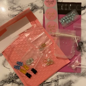 Staterkit  - Perfect startlistan om du vill börja sälja smycken innehåller: 1 Bubble mailer, 4 thank you klistermärken, 3 par örhängeskrokar silver, 2 par örhängeskrokar guld, 1 rosa postpåse, 6 gummibjörns berlocker (blå, svart, gul), 1 tygpåse, 13 ”vaxade” pärlor (ljusblå), 2 etiketter, 3 platta berlocker silver, 2 cellofanpåsar, 1 zippåse, 4 tass berlocker(guld silver), 4 klubb berlocker (rosa/brun). 