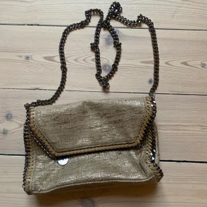 Stella McCartney falabella väska  - Crossbody väska i beige/guld tyg. Silvrig kedja med snap stängning. Köpt för ett par år sedan men i bra skick. Perfekt handväska där du får plats med det nödvändiga i och du ser storlek i förhållande till hörlurar Nypris 6500. 