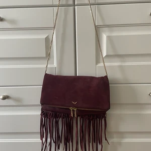 Zadig & Voltaire väska vinröd fransar - Unik och äkta vinröd Zadig & Voltaire väska som inte längre finns kvar. Guldig kedja som kan bäras både crossbody och under armen då kedjan kan göras kortare. Väl använd men i gott skick. Nypris ca 4000