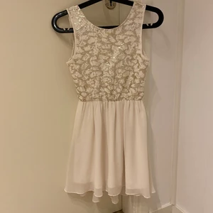 Finklänning vit/ljusrosa - Vit/ljuuuuuuust ljust rosa klänning, spets + beiga paljetter på överdelen av klänningen. Dragkedja baktill. Lappar bortklippta men uppskattar storleken till xs. Har några nopprar samt en pytteliten obehandlad fläck på kjolen. Superfin klänning som jag själv använt som nyårsklänning ett år.
