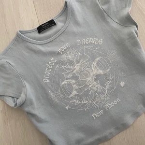 Ljusblå croptop med tryck - Söt ljusblå croptop köpt på bershka i storlek XS. Jag har vanligtvis S och denna sitter lite kort på mig som är ca 169cm men det beror på vad man föredrar. Fint skick! 50kr + frakt. 