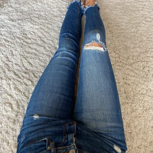 Jeans med slitsningar - Tighta jeans med riklig stretch. Slitningar över benen och fransade vid bensluten. Fin blå jeansfärg som håller vid tvätt. Sparsamt använda!