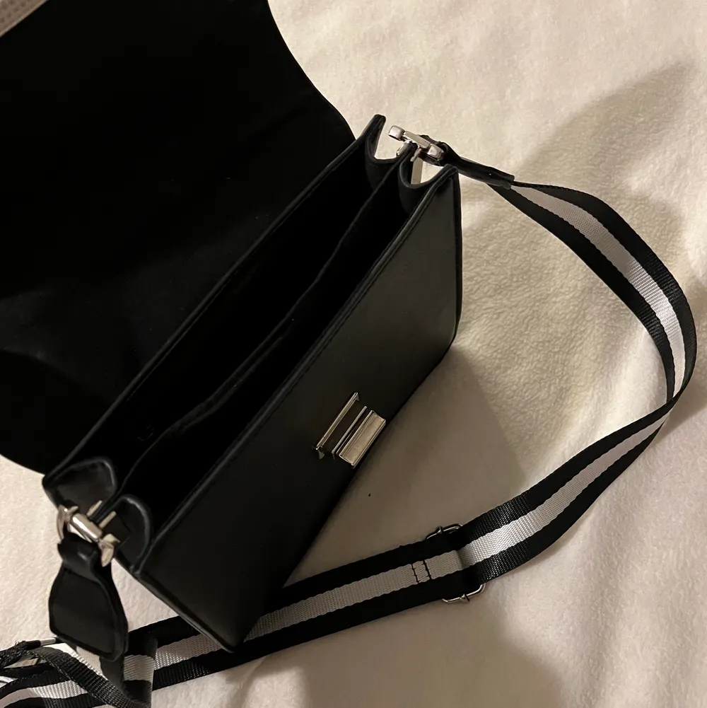 Snygg, svart, stilren handväska med ett ett randigt band som piffar upp den och outfiten! . Accessoarer.