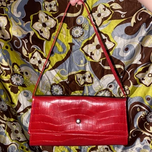 underbar röd baguetteväska!! - En jättefin röd baguette/90s väska!! Extremt bra kvalité och fina detaljer, bandet går att ta av helt och det finns tre fack i väskan-varav ett med dragkedja. Mönstret/materialet är jättecoolt och väskan känns väldigt lyxig - inga tecken på användning! Nypris 599kr, säljer för 150kr + 52kr frakt = 200kr totalt eller mötas i Uppsala!