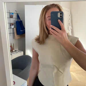 Beige topp från Ginatricot  - Säljer denna snygga beiga toppen med axelvaddar som man stänger med en dragkedja i ryggen. Den är ifrån Maja Nilsson Lindelöfs kollektion ihop med Ginatricot. Den är endast använd en gång och i mycket gott skick. Den är i storlek 34. Frakt tillkommer om inget annat är överenskommet 😊