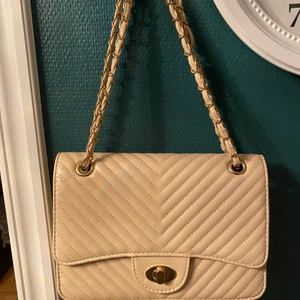 Beige väska helt ny  - -Handväska eller axelväska går att ha till båda👜  -Beige med guldiga detaljer på bandet -Man kan göra bandet både kort och långt  -Kan skickas 💌köparen betalar frakten -Står inte för postens slarv  -Aldrig använd  -Säljes då jag inte använder den -köparen får bestämma om det ska vara spårbar eller inte men står själv för posten😊💌