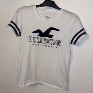 T-Shirt från Hollister storlek M  - Vit T-shirt med svarta detaljer från Hollister i storlek M men passar XS/S. Jättefin och skön till sommaren. I mycket bra kvalité. Säljes pga kommer ej till användning. 