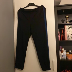 Svarta kostymbyxor i storlek S-M - Svarta kostymbyxor med blåa ränder på sidorna! Storlek S-M. Tyget är inte riktigt som vanliga kostymbyxor är.