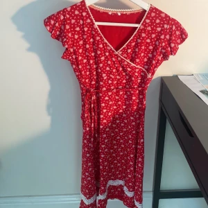 Röd blommig omlottklänning - Supersöt röd omlottklänning med vitt blommönster och volangärmar. Stod ingen storlek på klänningen eftersom lappen gått av, men är rätt säker på att det är xs!
