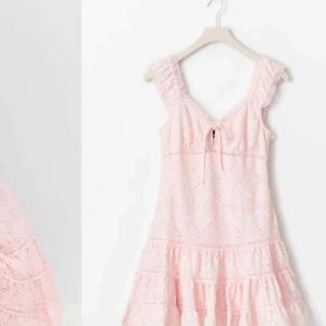 Söt ljusrosa spetsklänning med volang - Superfin ljusrosa kortklänning med broderad spets, volangkant nertill och breda axelband. V-ringad med knyt framtill och romantiska detaljer. Perfekt för sommarens alla tillfällen och ger en riktigt gullig vibe.