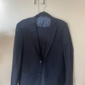 Mörkblå kostym Dressmann slim fit  - Säljer en stilren mörkblå kostym från Dressmann endast använd en gång.  Kavaj i storlek 48, slim fit. Byxor i storlek 31/32 slim fit. Nypris 1999kr