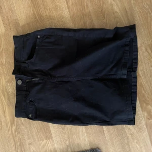 Svart jeanskjol med fickor - Svart jeanskjol med klassisk femficksdesign, bälteshällor och dragkedja framtill. Rak modell som slutar ovanför knäna, perfekt för en avslappnad och cool stil.