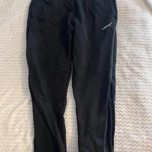 Svarta mjukisbyxor från Levis M - Svarta mjukisbyxor från Levis med knyt snöre i midjan och diskret Levis-logga på ena benet. Byxorna har en avslappnad passform och är tillverkade i mjukt material, perfekta för chill dagar eller när du vill vara bekväm. Vid eventuella funderingar är det bara att fråga!