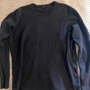 Mörkblå stickad tröja J.Lindeberg - Snygg mörkblå stickad tröja från J.Lindeberg med diskret strukturmönster. Tröjan har rund halsringning samt långa ärmar. Perfekt för dig som gillar stilrena och klassiska plagg med en modern twist. Knappt använd, kontakta för ytterligare funderingar!