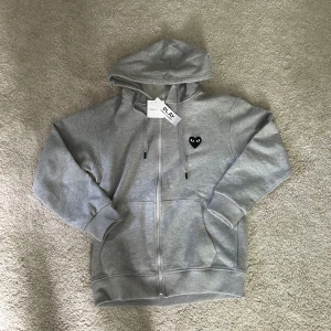 Comme des Garçons Play Hooded Zip - Comme des Garçons Play zip-hoodie – grå med svart hjärta Säljer en helt ny hoodie med dragkedja från Comme des Garçons Play. Klassisk modell med det svarta hjärtat med ögon på bröstet. Endast provad – passade tyvärr inte mig.  ✔️ Storlek: M ✔️ Färg: Grå ✔️ Skick: Helt ny  Skicka meddelande vid frågor eller om du vill ha fler bilder!