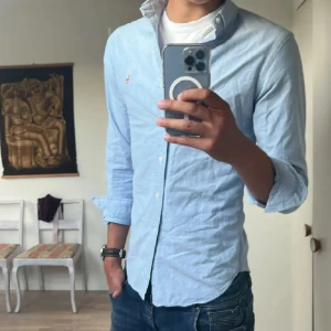 Ralph Lauren Skjorta (pris diskuterbart) - !! NY SKICK !! Klassisk ljusblå skjorta från Ralph Lauren i SLIMFIT med button-down krage och broderad logga på bröstet. Skjortan har lång ärm, smal passform och är tillverkad i mjuk bomull. Perfekt för en clean och stilren look. Storlek 20 sitter Som S-M