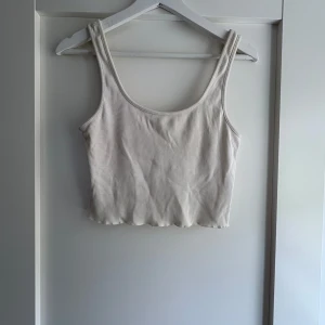 Ribbad vit croppad linnetopp - Säljer en stilren croppad linnetopp i ribbad vit bomull. Toppen har breda axelband och en rundad halsringning, perfekt för en chill och enkel look. Passar snyggt till både jeans och kjol. Superskön och lätt att matcha med allt.