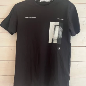 Svart Calvin Klein Jeans t-shirt XS - Svart t-shirt från Calvin Klein Jeans i bomull med vit text och grafiskt tryck framtill. Klassisk passform med rund hals och korta ärmar. Snygg och stilren med New York-tryck och CK-logga på framsidan.