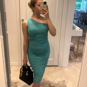 Turkos one shoulder klänning HELT NY  - Snygg turkos klänning med one shoulder-design och tight passform. Klänningen är draperad och har en midilängd som sitter figurnära. Köpt från NAKD, prislapp kvar som ny. Jättesmickrande på kroppen. 