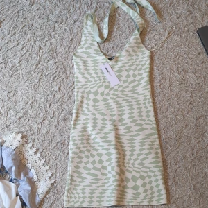 Grön och vit mönstrad kortklänning - Superfin kortklänning från Gina Tricot med grönt och vitt grafiskt mönster. Klänningen har smala axelband som knyts i nacken och en snygg v-ringning. Perfekt för dig som gillar trendiga och unika plagg med coola detaljer.