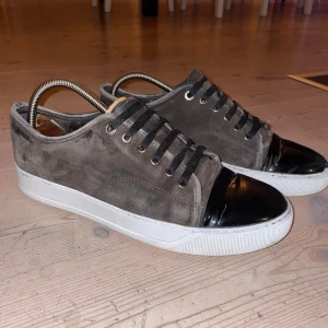 Lanvins - Snygga sneakers från Lanvin i brun mocka med svart lackad tå och vita sulor. Skorna har mörk bruna snören och en klassisk låg profil. Perfekta för dig som gillar stilrena detaljer och exklusiv känsla. Passar till allt. 