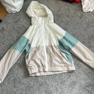 Pastellfärgad vindjacka från McKinley - Snygg vindjacka från McKinley i pastelliga färger – vit, beige och ljusblå. Jackan har huva, dragkedja framtill och två fickor. Perfekt för blåsiga dagar och enkel att matcha med det mesta. Lätt och smidig att ta med sig överallt.