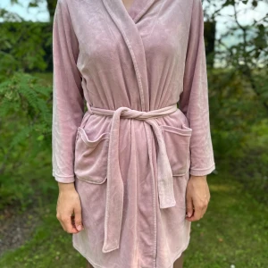 Rosa cardigan jacka med brodyr - Mysig ljusrosa cardigan jacka i mjukt material med broderad text och ögon på ryggen. Omlottmodell med knytband i midjan och stora fickor framtill. Perfekt för chill dagar hemma.