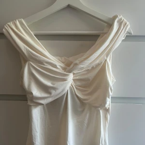 Vit omlott topp från H&M - Supersnygg vit off-shoulder topp från H&M med omlott-detalj. Toppen är tillverkad i mjukt, glansigt material som ger en lyxig känsla. Helt oanvänd med prislappen kvar perfekt topp både till vardags och till lite finare fester/middagar. 