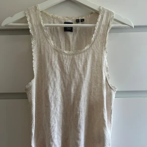 Beige ribbad linnetopp från Superdry - Säljer en beige ribbad linnetopp från Superdry. Toppen är ärmlös och har fina spetsdetaljer längs kanterna. Perfekt för varma dagar och enkel att styla med dina favoritjeans eller kjol.