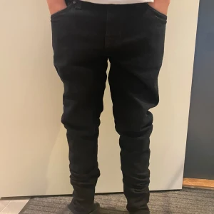Svarta jeans från Nudie Jeans, 27/30 - Säljer ett par svarta jeans från Nudie Jeans i modellen 27/30. Jeansen har klassisk femficksdesign, raka ben och snygga detaljer på bakfickorna. Perfekta för dig som gillar en stilren och enkel look.