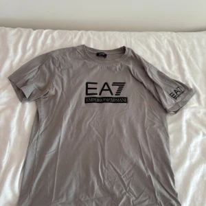 Grå EA7 Emporio Armani t-shirt - Snygg grå t-shirt från EA7 Emporio Armani med svart logga på bröstet och ärmen.  Är du intresserad av plagget är de bara att skriva.  Vill du ha billigare genom bundle eller lika feta kläder kolla bara in min profil och gör ett bundle och skriv till mig. M/L
