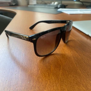 Svarta Ray-Ban boyfreind solglasögon - Klassiska Ray-Ban Wayfarer solglasögon med svart båge i plast och bruna tonade glas. Snygg och tidlös modell med Ray-Ban-logga i guld på skalmarna. Perfekta för att lyfta din stil under soliga dagar.