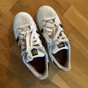 Adidas Superstar vita sneakers - Adidas Superstar sneakers i vitt skinn med svarta ränder och svart häl. Fräscha och kan såklart diskutera priset❤️