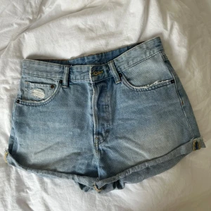 Högmidjade blåa jeansshorts - Snygga ljusblå jeansshorts från H&M med hög midja och avslappnad passform. Shortsen har slitna detaljer både fram och bak, klassiska fem fickor och uppvikta benslut. Perfekta för varma dagar och en chill look