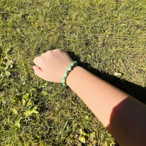 Grönt pärlarmband med blomma - Supergulligt armband med gröna och vita pärlor samt en liten blomdetalj i mitten. Perfekt accessoar för dig som vill ha något färgglatt och lekfullt på handleden. Stretchig modell som passar de flesta handleder. Vi har 1 av denna sort.