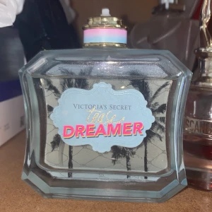 Victoria's Secret Tease Dreamer parfym - Snygg parfymflaska från Victoria's Secret, Tease Dreamer. Flaskan är rektangulär i tjockt, transparent glas med palmmotiv och blå etikett. Korken har guldiga detaljer och en pastellfärgad ring. Perfekt för dig som gillar fräscha och tropiska dofter. Har tappat bort saken man sprejar med men kan lägga på en om de behövs ;)  Luktar otroligt gott men har redan flera parfymer så denna kommer ej till användning har krämen till men den är lite konstig men luktar tvär gott också 🥹🫶🏻köpte den för 650 kr