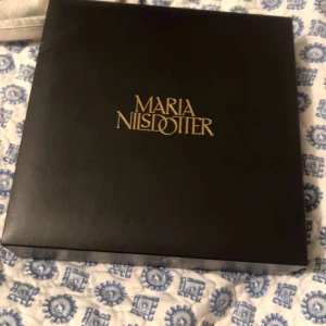 Pärlhalsband från Maria Nilsdotter - Unikt halsband från Maria Nilsdotter med chunky silverkedja och sju vita pärlor i mitten. Kedjan har en cool säkerhetsnål-detalj och justerbar längd. Perfekt statement piece för dig som gillar edgy men elegant stil. Nypris 6500 