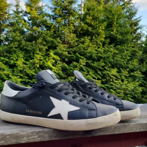 Golden Goose  - Golden Goose Superstar sneakers i svart skinn med vit stjärna på sidan och vit häl. Klassisk låg modell med svarta snören och vit sula. Snygg streetstil med tydliga logodetaljer på plös och innersula. Perfekta för dig som gillar en clean men edgy look. Är nog äkta men inte helt 100 pågrund av att jag köpte av en annan kille för 2300 dustbag medföljer / tvättas