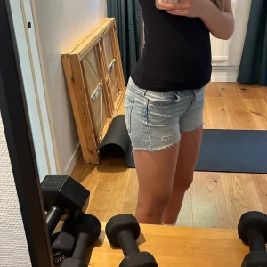 Ljusblå jeansshorts med slitningar - Säljer ett par ljusblå jeansshorts med slitna detaljer framtill. Klassisk femficksmodell med bälteshällor.