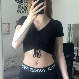 Svart croppad topp med snörning FB Sister - Superskön svart croppad topp i strl XS från FB Sister med korta ärmar och v-ringning. Toppen har ribbad struktur och snygg snörning framtill som ger möjlighet till justering💕Sparsamt använd.