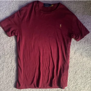 Vinröd t-shirt Polo Ralph Lauren - Og pris: 959kr Säljer för: 299kr Vinröd t-shirt från Polo Ralph Lauren i slim fit-modell. Klassisk design med rund hals och broderad polospelare på bröstet. Skön bomullskvalitet som passar perfekt till jeans eller shorts. Enkelt och stilrent plagg för dig som gillar snygga basics.