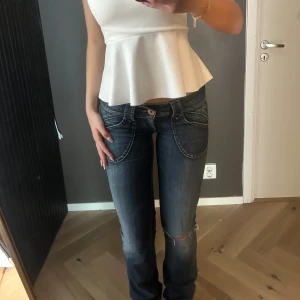 Lågmidjade blå jeans med slitning - Säljer ett par blå jeans med låg midja och raka/utsvängda ben. Jeansen har markerade sömmar, stora fickor fram och en snygg slitning på ena knät. Storleken är 27x34 och passar mig i längden som är 177, men passar även om man är kortare💖