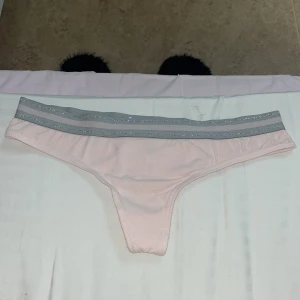 2-pack stringtrosor i rosa och grått - Två par stringtrosor i mjuk bomull, ett par ljusrosa och ett par ljusgrå. Båda har bred resår i midjan med glittrig silverdetalj för en snygg och sportig look. Perfekta för dig som gillar bekväma och stilrena underkläder. Är i storlek M. Oanvända o nya