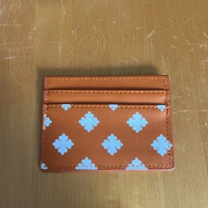 Orange kortfodral med vit mönster - Snyggt orange kortfodral med vita grafiska mönster. Perfekt för att hålla koll på dina kort och cash i fickan eller väskan. Stilren och smidig design som sticker ut. Aldrig använt!!