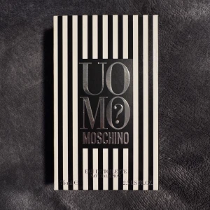 Moschino Uomo? Eau de Toilette 75ml - Moschino Uomo? Eau de Toilette i en stilren glasflaska med silverfärgad metallkork. Parfymen kommer i en svartvit randig kartong med metallic text. Flaskan rymmer 75 ml och har en klassisk, maskulin design med tydlig Moschino-logga.